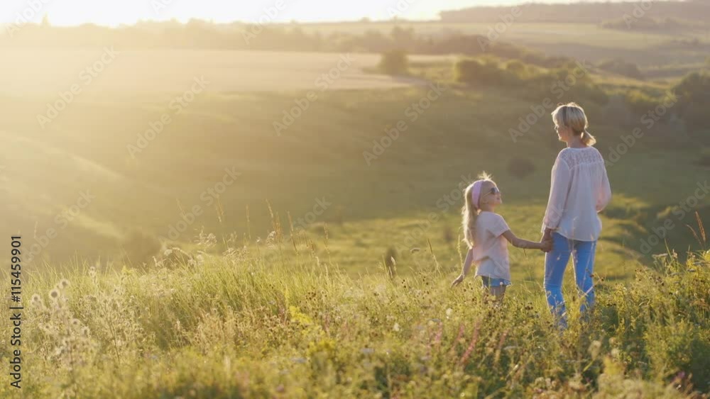 Mum with a daughter of 5 years on a large hill, watching the sunset Mum with a daughter of 5 years on a large hill, watching the sunset