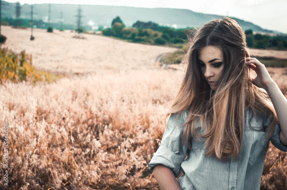 Fototapeta premium Beautiful and young girl in a man's shirt standing in the field. shirt for the girl. Nature. Wind inflates hair.