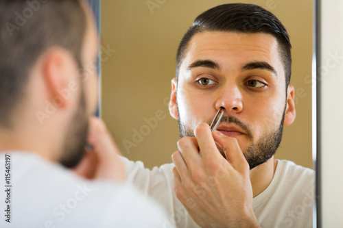 Handsome man remove hair with pincers.