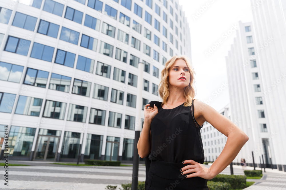 Blond woman in black standing near white buildings