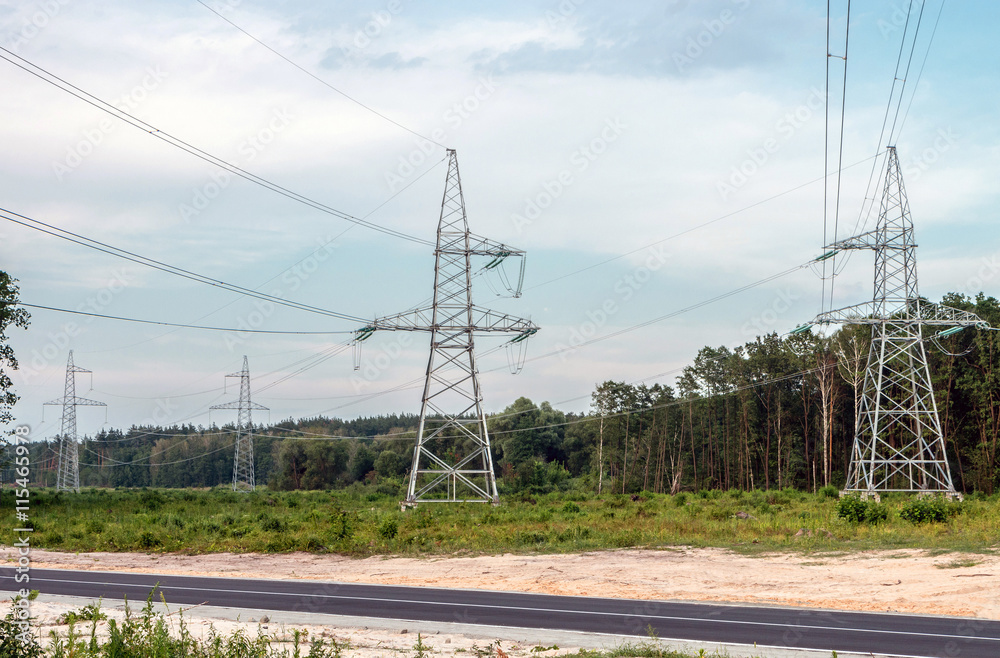 Fototapeta premium Electricity pylons with wires on a background of forest and roads.