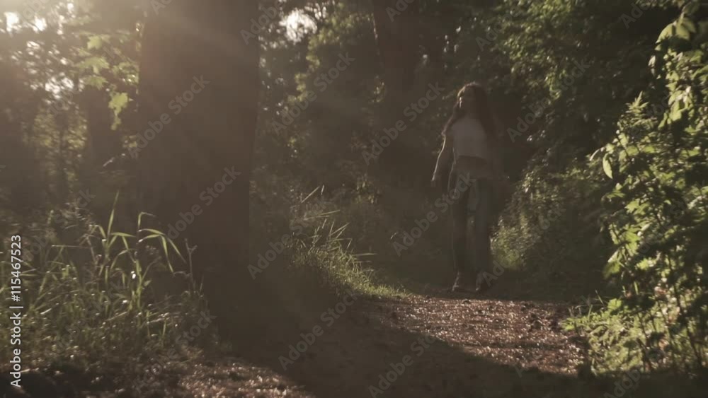 Brunette girl walking towards camera in sunset coniferous forest. Zoom out slow motion shot. Bleached colors Brunette girl walking towards camera in sunset coniferous forest. Zoom out slow motion shot. Bleached colors
