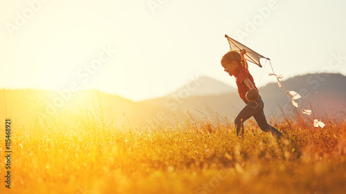 happy child girl with a kite running on meadow in summer photo
