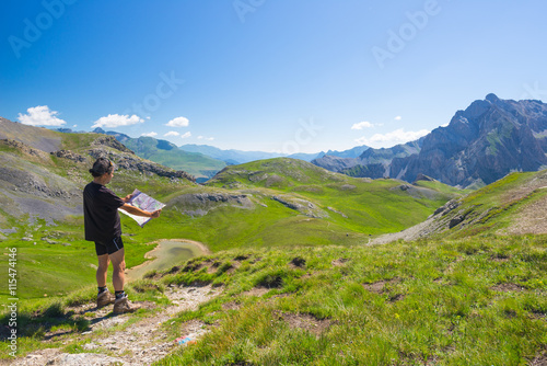 Hiker reading trekking map while resting at panoramic mountain spot. Outdoors activities, summer adventures and exploration on the Italian French Alps. Expansive view from the top. © fabio lamanna