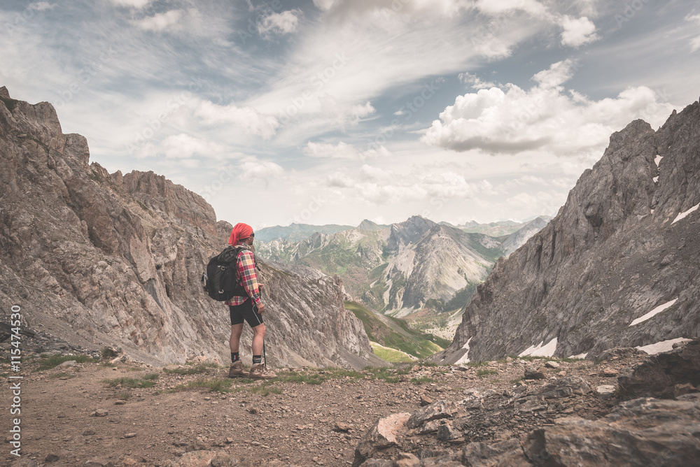 Backpacker hiking on footpath and looking at expansive view from the top. Summer adventures and exploration on the Italian French Alps. Toned retro vintage styled image.