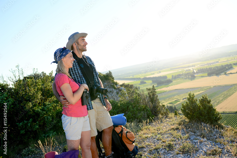 young couple with backpack on adventure mountain trek admiring a beautiful sunset landscape