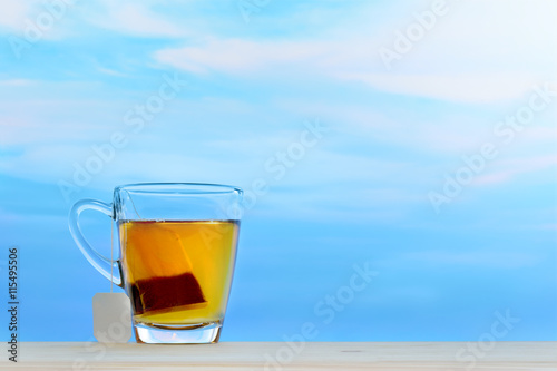 Cup of tea with tea bag on sky background