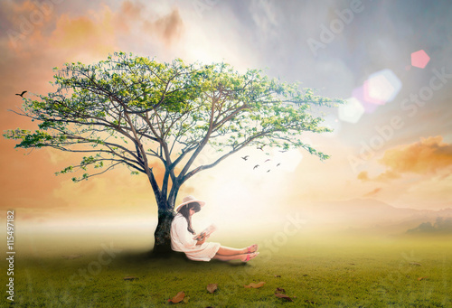 Read a book day concept: Asian girl reading fantastic book under big tree in autumn sunset background