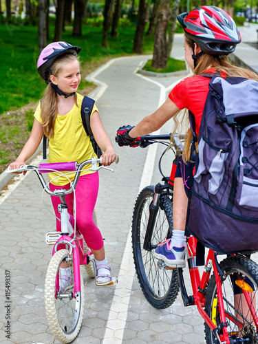 Bikes bicyclist girl. Girls wearing bicycle helmet and glass with rucksack ciclyng bicycle. Girls children cycling meet on white bike lane. photo