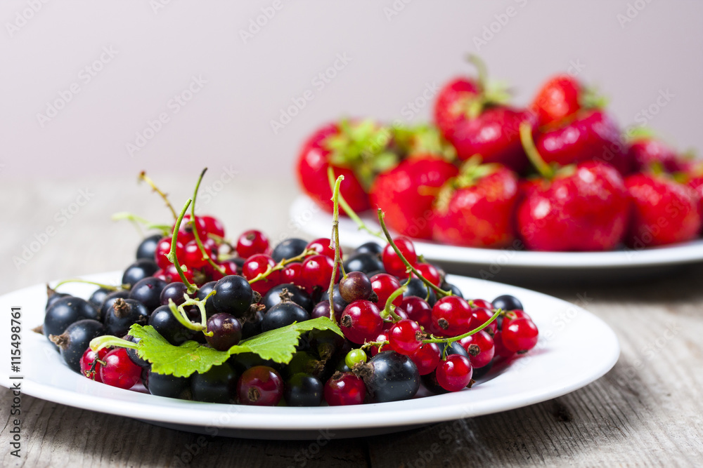 Plates with fresh picked strawberries and black and red currants Plates with fresh picked strawberries and black and red currants