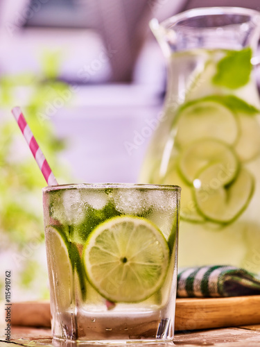 Country drink. On wooden boards is glass jug with transparent drink and lime glue bowl. A drink number seventy eight with ice cubes . Country life. Light background.