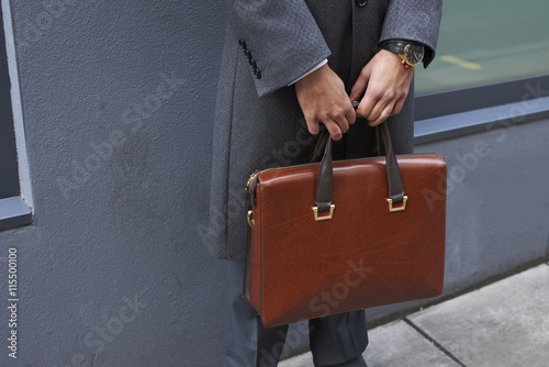 Midsection of man holding briefcase while standing outdoors