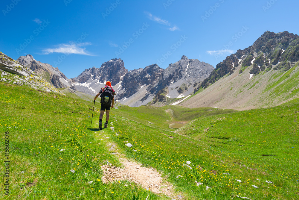 Backpacker hiking on footpath and looking at expansive view from the top. Summer adventures and exploration on the Italian French Alps.