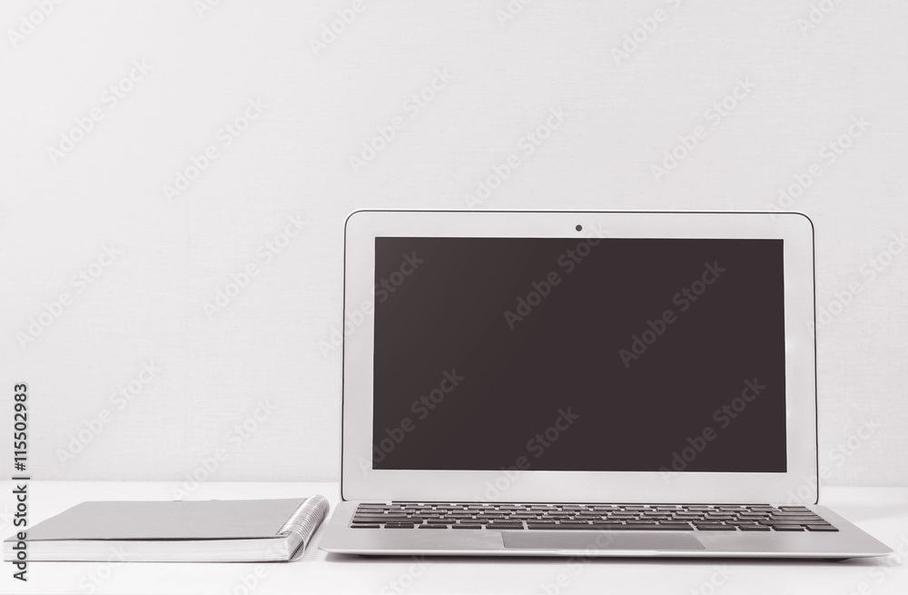 Closeup computer notebook on blurred white wood desk and cream color wallpaper wall in room texture background , beautiful work place interior of house concept in black and white tone
