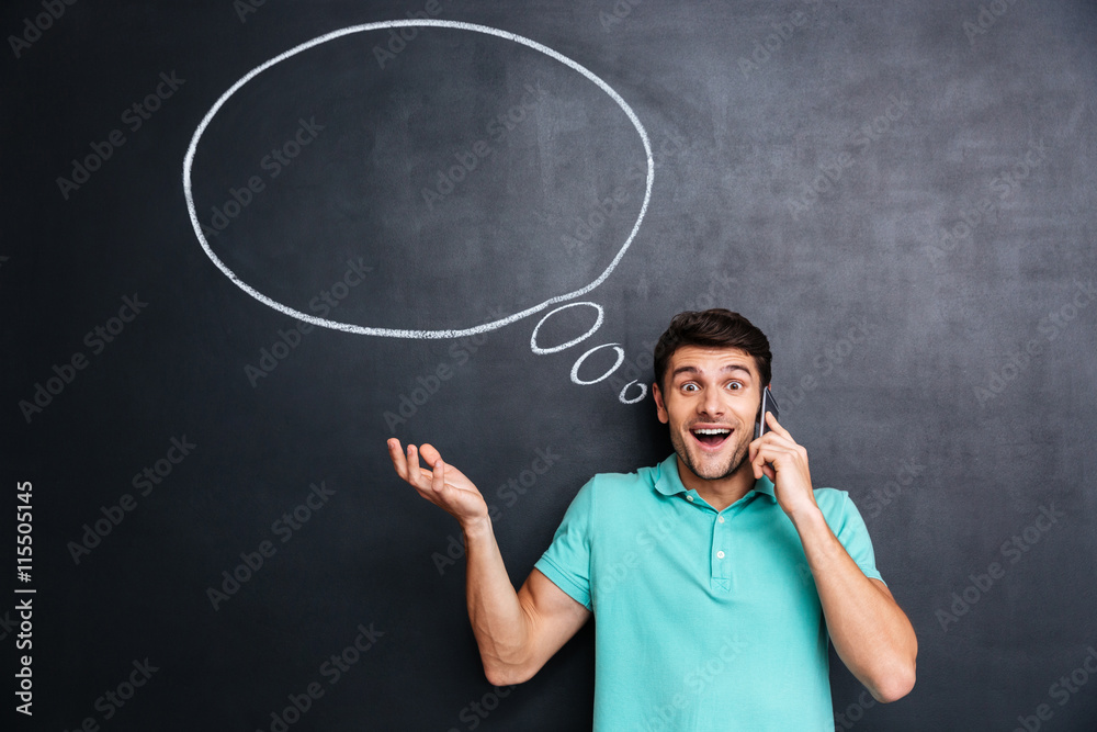 Surprised young man talking on mobile phone over blackboard background