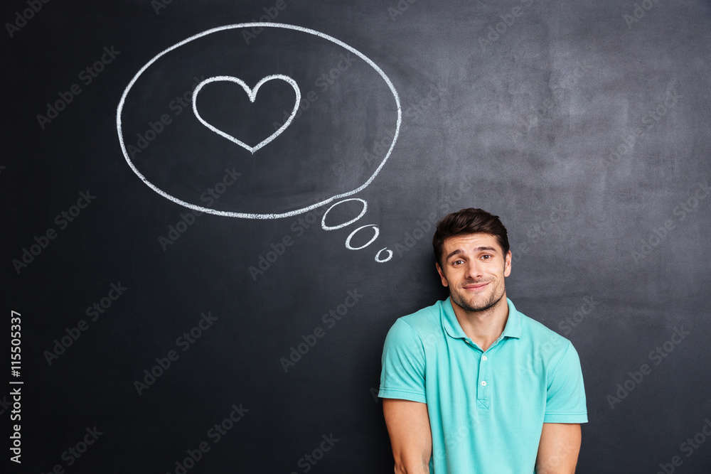 Shy cute young man thinking about love over blackboard background