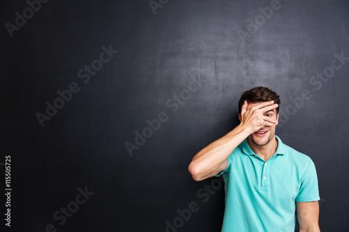 Casual man covering his eyes with fingers over black background