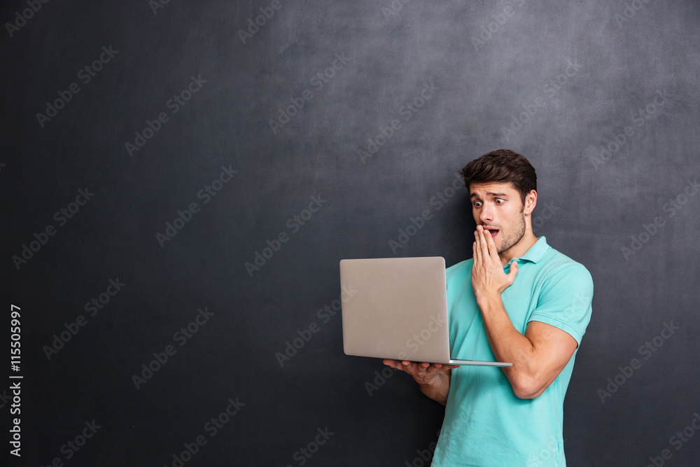 Naklejka premium Amazed shocked young man standing and using laptop