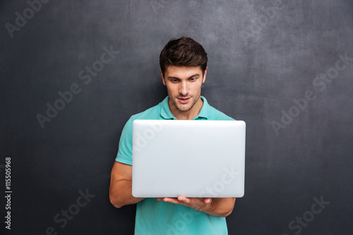 Concentrated handsome young man standing and using laptop