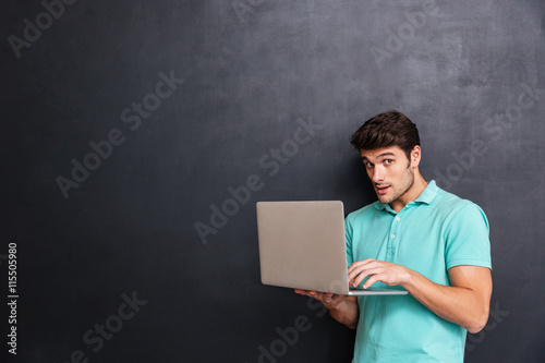 Scared suspicious young man standing and usong laptop photo