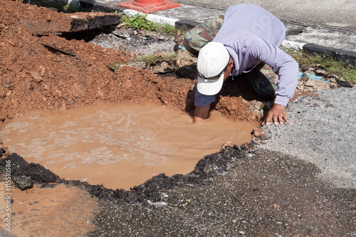 Male workers repair pipe water main broken, tube underground water on road.