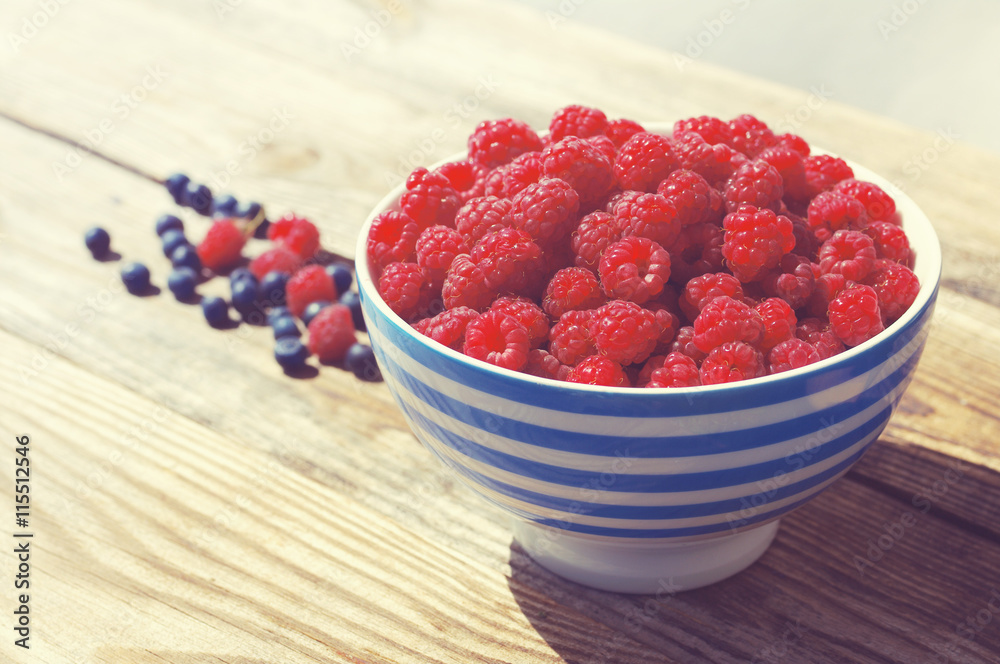 Mature juicy berries of raspberry and bilberry in a plate on a wooden table Mature juicy berries of raspberry and bilberry in a plate on a wooden table