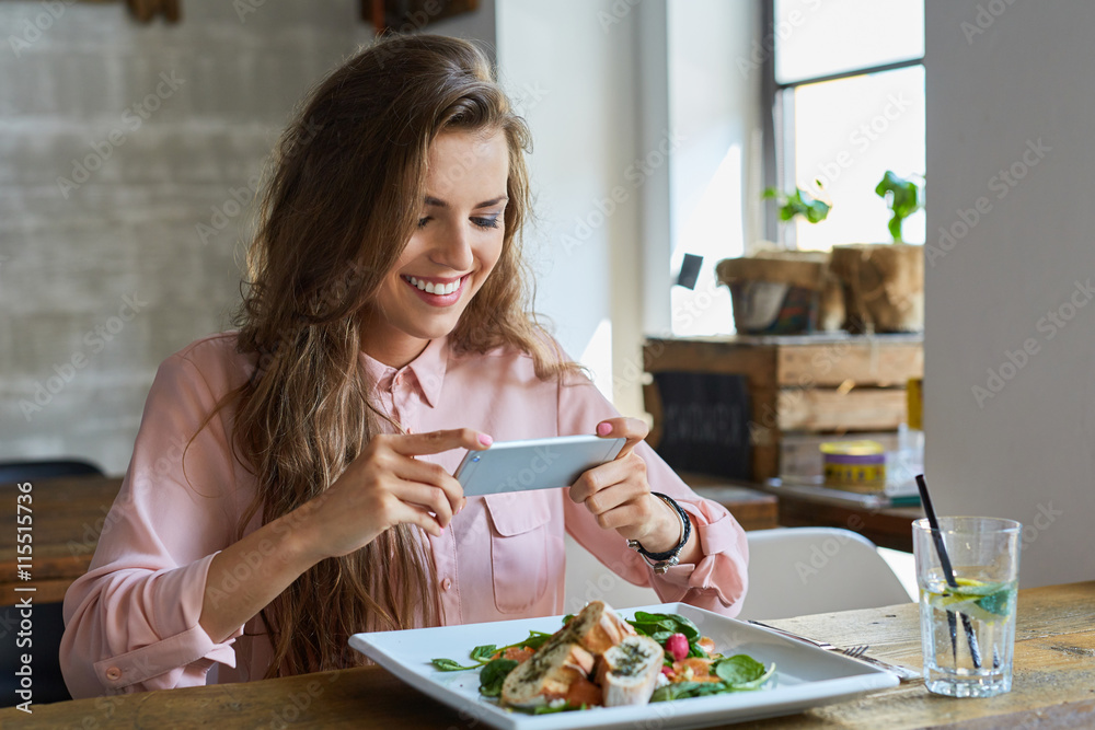 Female blogger photographing lunch in restaurant with her phone