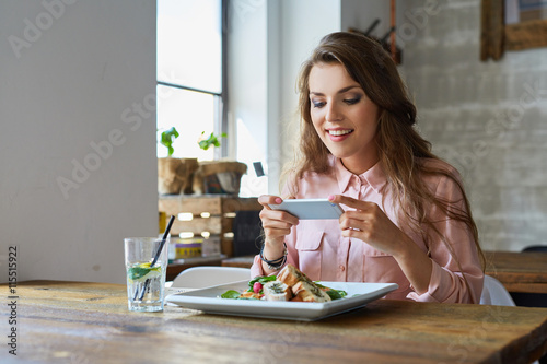 Young woman photographing her meal in restaurant photo