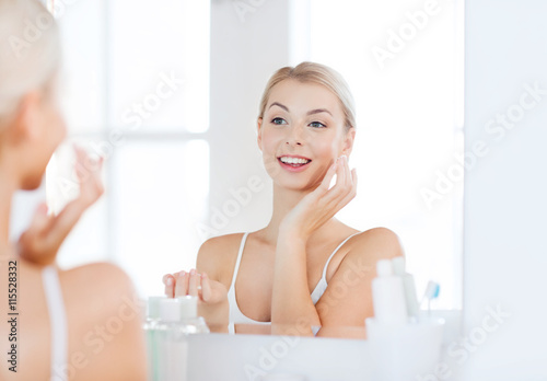 happy woman applying cream to face at bathroom