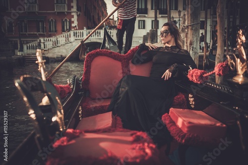 Beautiful woman in black dress with carnaval mask riding on gondola. 