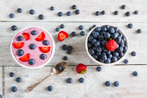 Breakfast bowl with yougurt, muesli, fresh blueberries and strawberries. Light wooden background, top view.