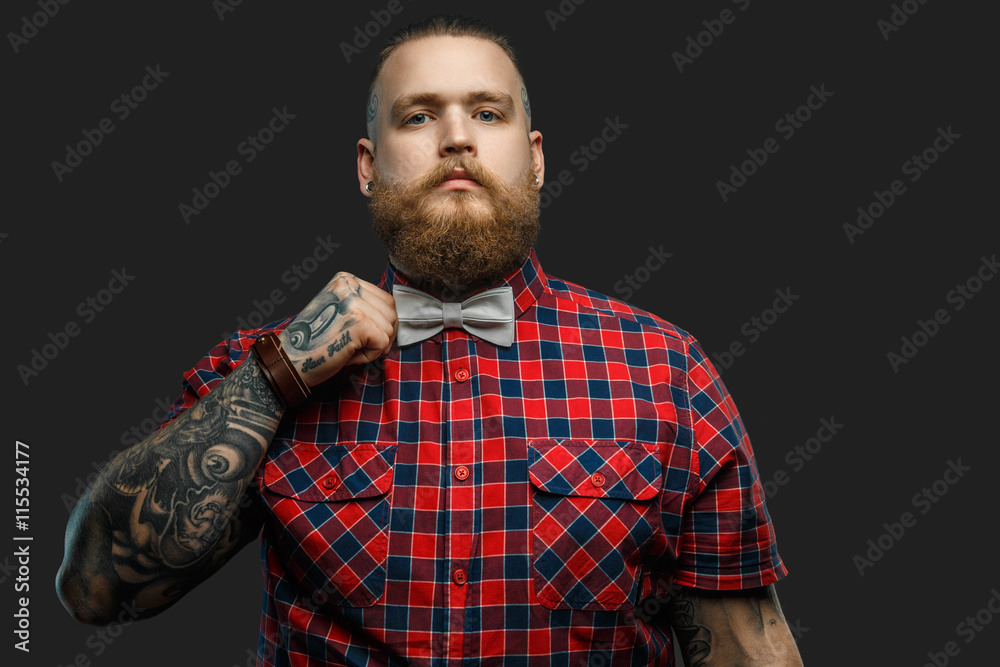 Tattooed bearded unformal male in red shirt and grey bow tie. Stock Photo