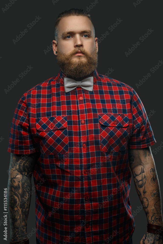 Tattooed bearded unformal male in red shirt and grey bow tie. Tattooed bearded unformal male in red shirt and grey bow tie.