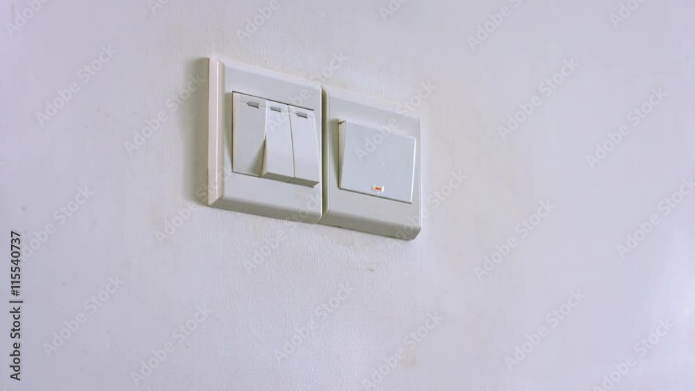 A man's right hand reaches out to press a wall switch with his thumb, turning on the lights, with sound.