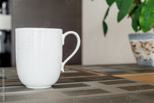 Morning white cup of coffee or tea on a wooden kitchen table with a plant on a background. Dark brown colors. Focus at handle