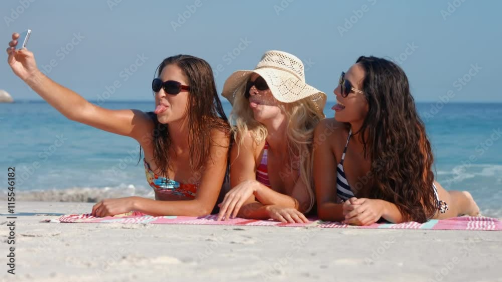 Video of happy pretty friends lying on towel and taking a selfie at the beach Video of happy pretty friends lying on towel and taking a selfie at the beach