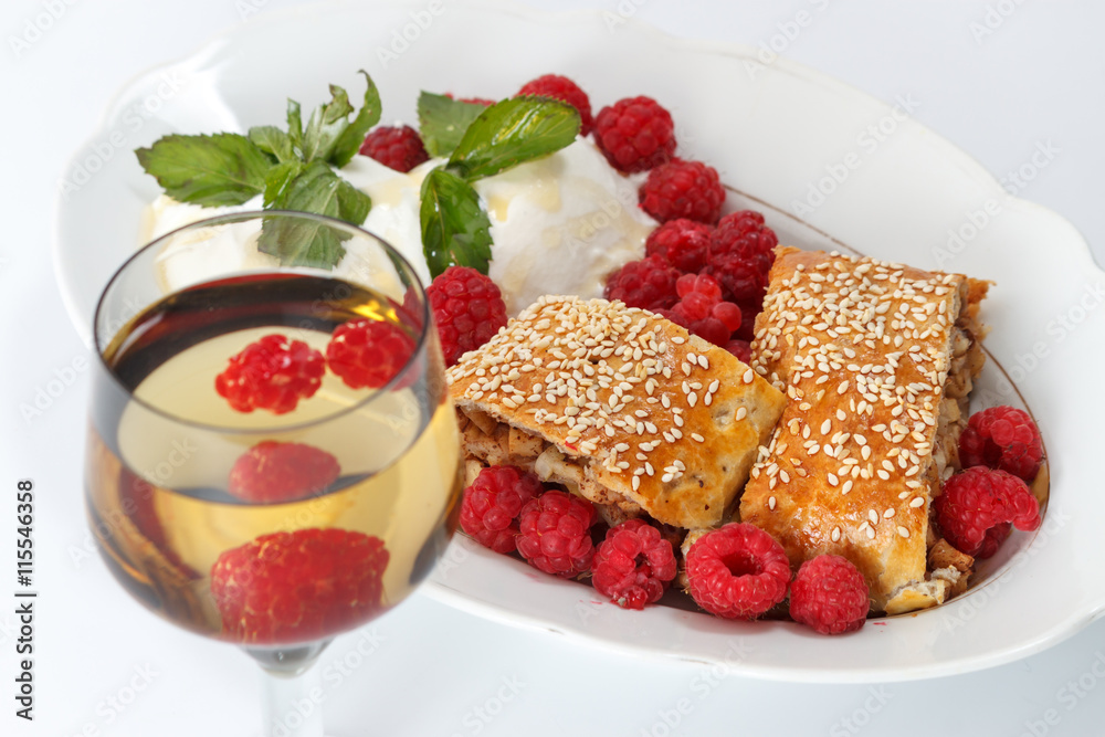 Piece of traditional apple strudel pie served with ice-cream, fresh mint, raspberry and glass of wine Piece of traditional apple strudel pie served with ice-cream, fresh mint, raspberry and glass of wine