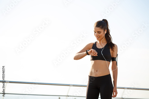 Fototapeta Naklejka Na Ścianę i Meble -  Picture of young fitness girl looking on watch with sea background