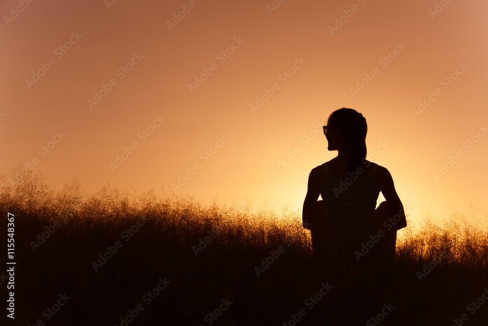 Young woman sitting in a field watching the sunset.
Young woman sitting in a field watching the sunset.