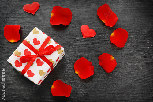 Gift box, rose petals and decorative hearts on wooden background
