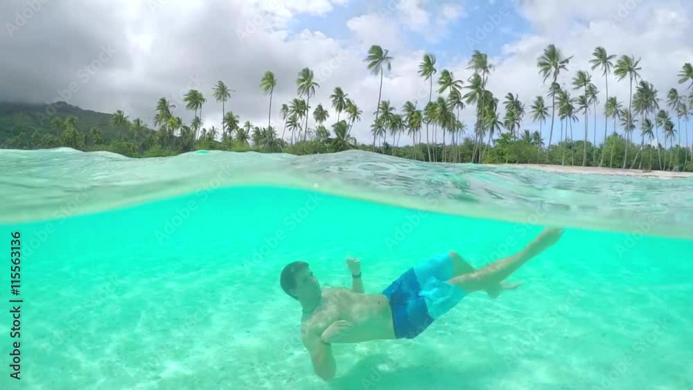 UNDERWATER: Young man in swimsuit swimming in perfect island lagoon UNDERWATER: Young man in swimsuit swimming in perfect island lagoon