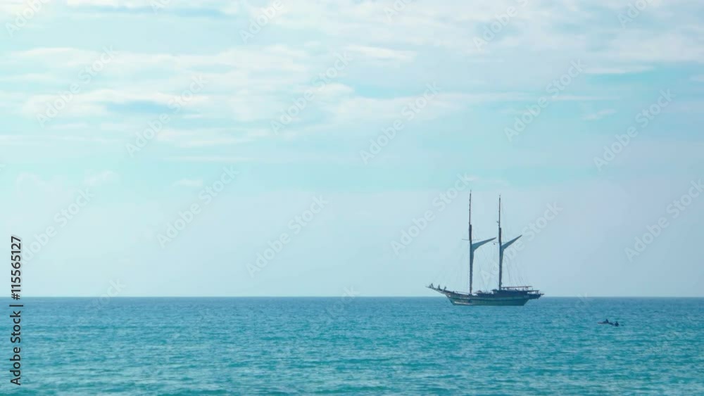 Two masted, wooden sailing yacht, anchored on the horizon off a popular tropical beach in Southeast Asia. Two masted, wooden sailing yacht, anchored on the horizon off a popular tropical beach in Southeast Asia.