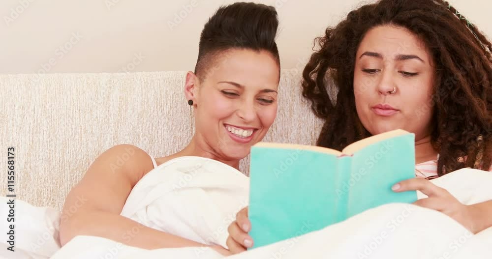 Smiling lesbian couple reading book in the bed at home Smiling lesbian couple reading book in the bed at home