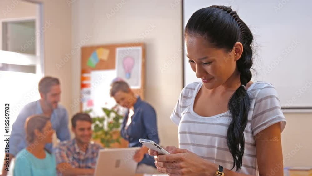 Casual businesswoman texting with her colleagues behind her