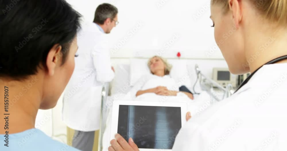 Doctors studying xrays on tablet in front of sick patient in bed Doctors studying xrays on tablet in front of sick patient in bed