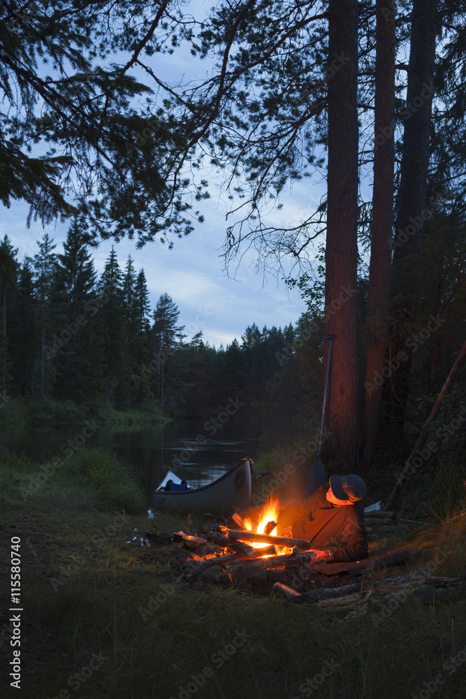 Sweden, Vastmanland, Svartalven, Man by bonfire on riverbank Sweden, Vastmanland, Svartalven, Man by bonfire on riverbank