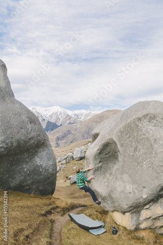 New Zealand, Castle Hill, Young man climbing up boulder with snowcapped mountains seen in distance photo