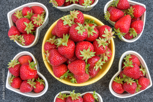 Fresh picked strawberries in a yellow bowl  and white heart shaped bowls  on a gray background  