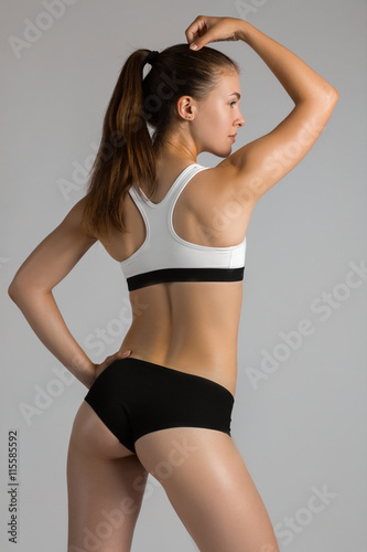 Beautiful super fit young woman showing off her perfect muscular body. Fitness model training with dumbbell . Slim sturdy back muscles. Studio shot