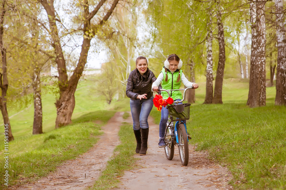 happy mother teaches his daughter to ride a bike. A mother is glad to successes of daughter happy mother teaches his daughter to ride a bike. A mother is glad to successes of daughter